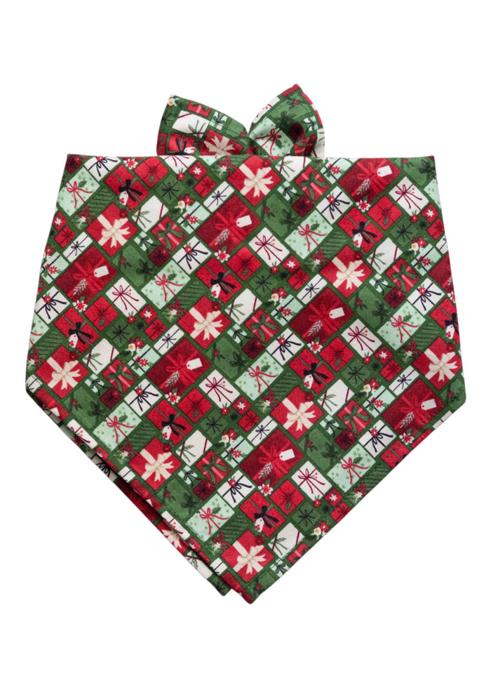 Dog bandana made from fabric printed with a tightly packed grid of holiday gift boxes in festive colors. Each box features different wrapping styles, bows, and tags, arranged in a diagonal plaid-like pattern. The bandana is folded in a triangular shape with pointed ends for tying.