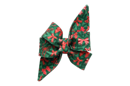 Large decorative dog belle bow made from green fabric printed with bows, gingham ribbon designs, and candy canes. The feminine belle bow features exaggerated, pointed tails and layered loops, creating a dramatic holiday look, ideal for attaching onto a collar as a festive accessory.
