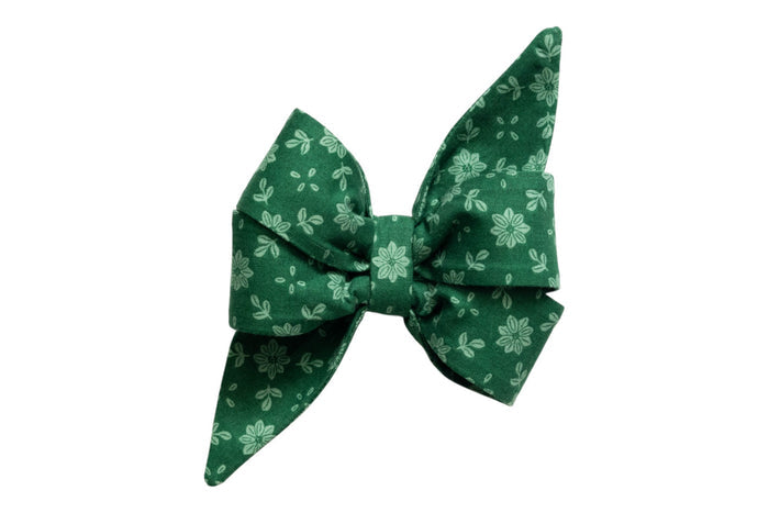 Floral dog belle bow accessory with a voluminous shape and extended, pointed ends. Made from green fabric adorned with light green flowers and leaf motifs, the belle bow is ideal for attaching to a collar for a stylish and festive appearance.