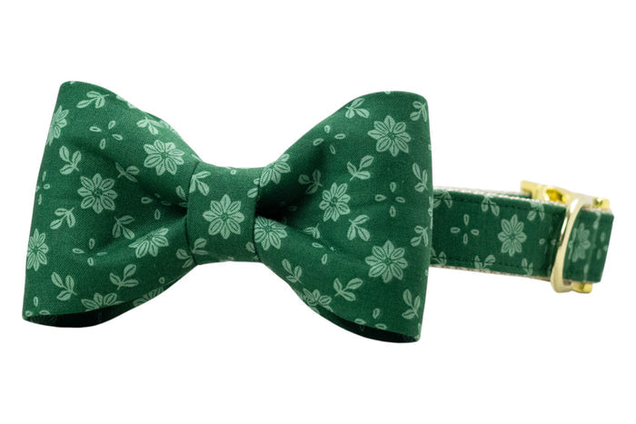 Green floral dog collar with a centered bow tie, crafted from matching fabric printed with pale green flowers and leaves. The bow tie has a crisp, symmetrical design, and the collar is fitted with shiny hardware, including an adjustable buckle.