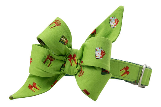 Festive dog collar in light green with a large, structured belle bow attached, both covered in a whimsical print of colorful wrapped presents. The feminine belle bow features exaggerated loops and pointed ends for a playful holiday look, and the collar includes an adjustment buckle.