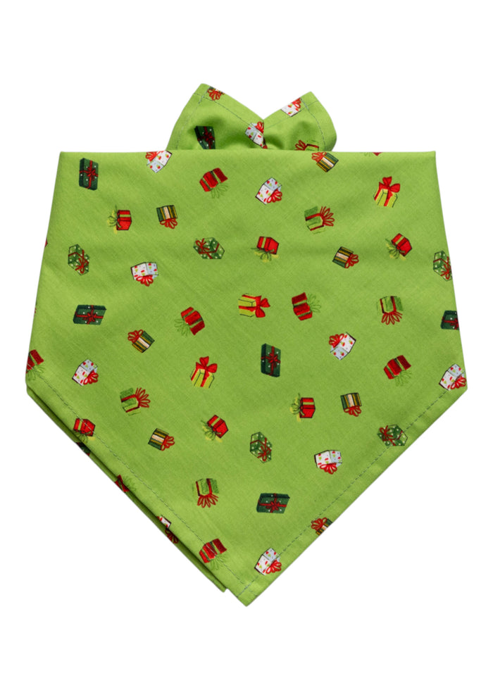 Festive green dog bandana adorned with a colorful all-over print of small gift boxes in festive colors, each tied with ribbon. The fabric is folded into a triangular shape with two upper ties, making it easy to wrap around the neck for a cheerful holiday look.