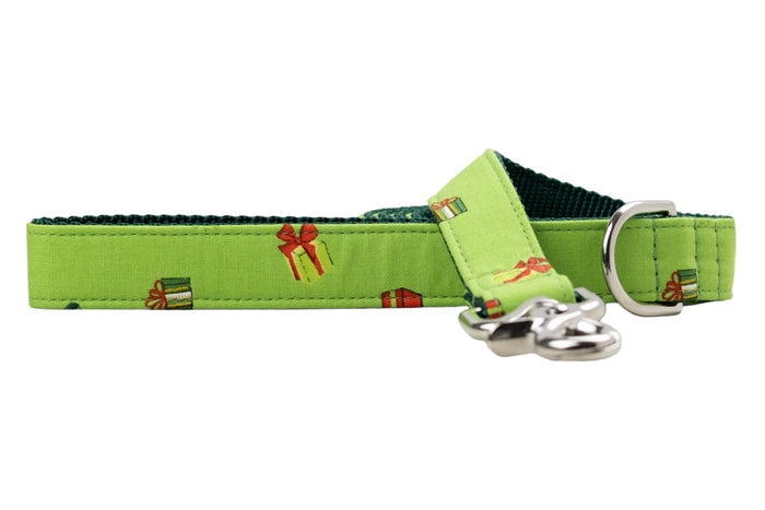 Festive green dog leash printed with a scattered pattern of tiny gift boxes in various colors and bow styles. Constructed with a sturdy green woven lining and metal hardware, the leash includes a metal D-ring near the handle and a clasp.