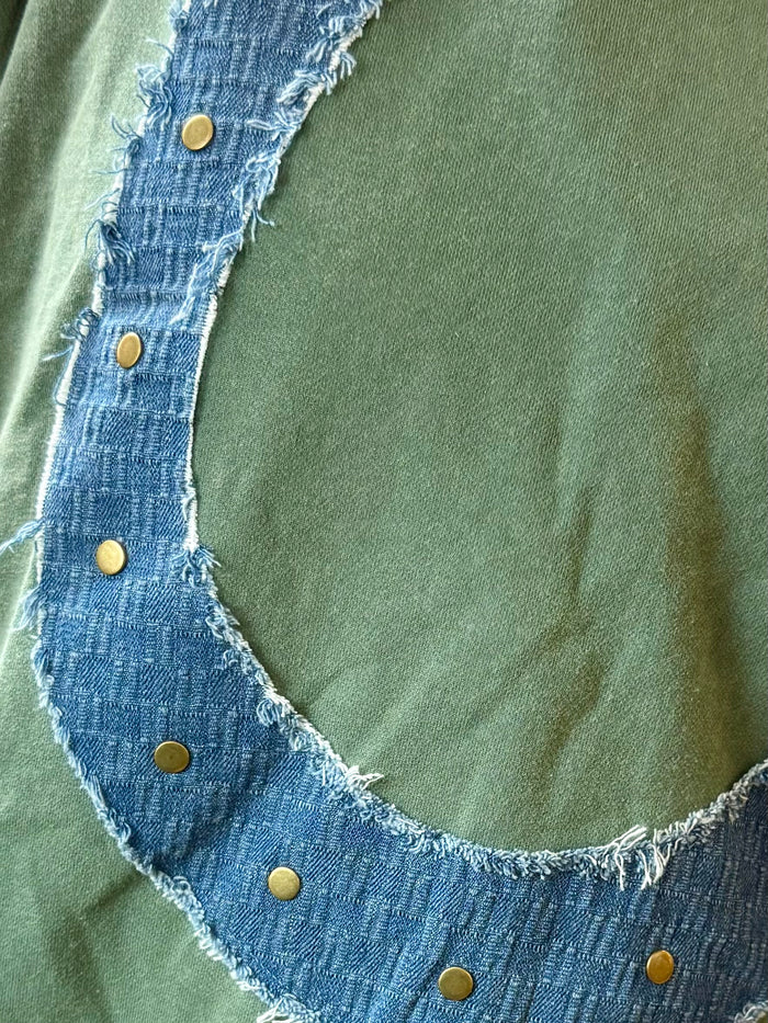 Green sweatshirt front with horseshoe denim patch and small gold stud accents