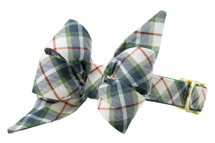 Dog collar with an attached oversized matching belle bow in a light fabric featuring a tartan plaid pattern, accented by thin diagonal stripes. The belle bow has two long, pointed tails for a stylish, festive look. The collar includes a polished D-ring and adjustable buckle for secure fit.