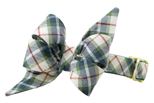 Dog collar with an attached oversized matching belle bow in a light fabric featuring a tartan plaid pattern, accented by thin diagonal stripes. The belle bow has two long, pointed tails for a stylish, festive look. The collar includes a polished D-ring and adjustable buckle for secure fit.