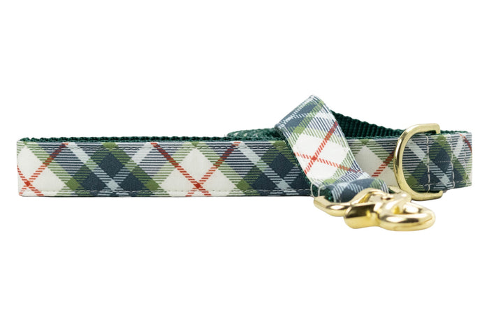 Dog leash with a tartan plaid pattern in olive green, accented with thin diagonal lines. The leash features durable green webbing on the underside, a metal swivel clasp, and a matching D-ring near the handle.