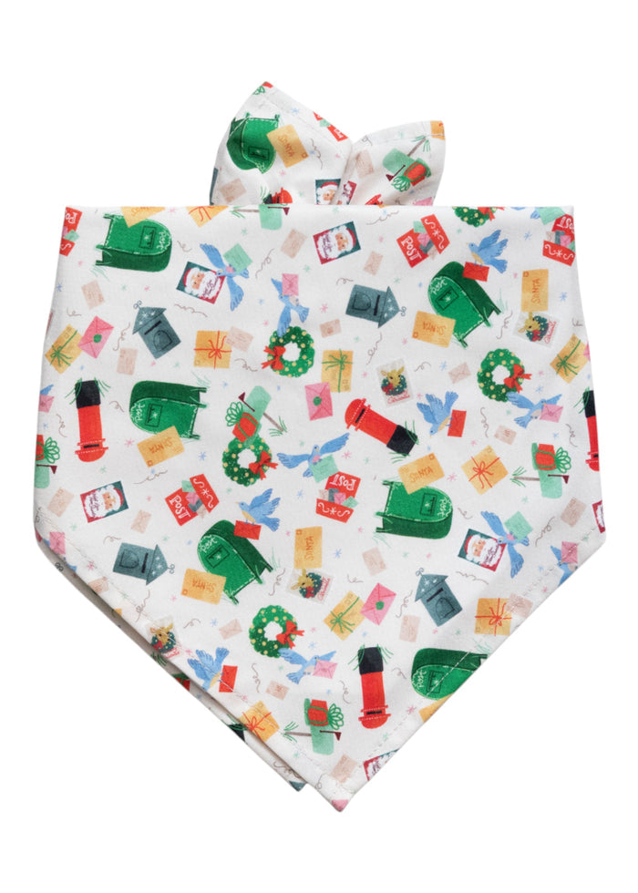 Festive dog bandana with a light background printed with whimsical holiday mail illustrations, including letters, wrapped presents, vintage-style mailboxes, postage stamps with Santa, and holiday wreaths. The bandana has a classic shape, designed to be tied at the neck.