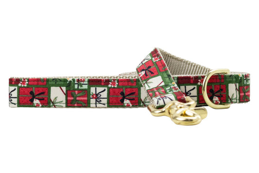 Holiday-themed dog leash featuring a repeating print of square gift boxes in classic Christmas colors. Each box is detailed with ribbons, tags, holly, or pine accents, creating a tightly packed pattern. The leash is backed with nylon webbing and includes metal hardware.